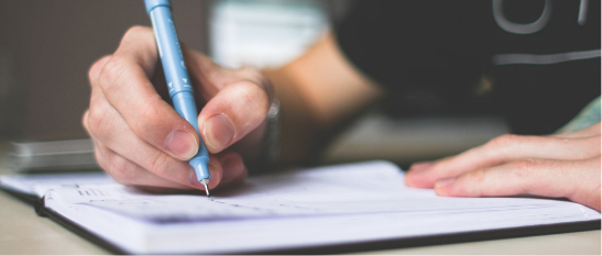 A hand holding a pen writing in a notebook