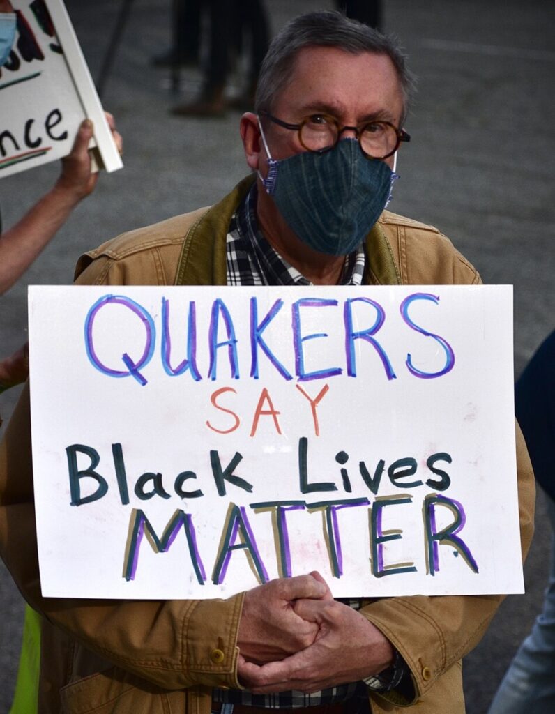 Un hombre que lleva una máscara facial porta un cartel hecho a mano que dice "Los cuáqueros dicen que las vidas negras importan".