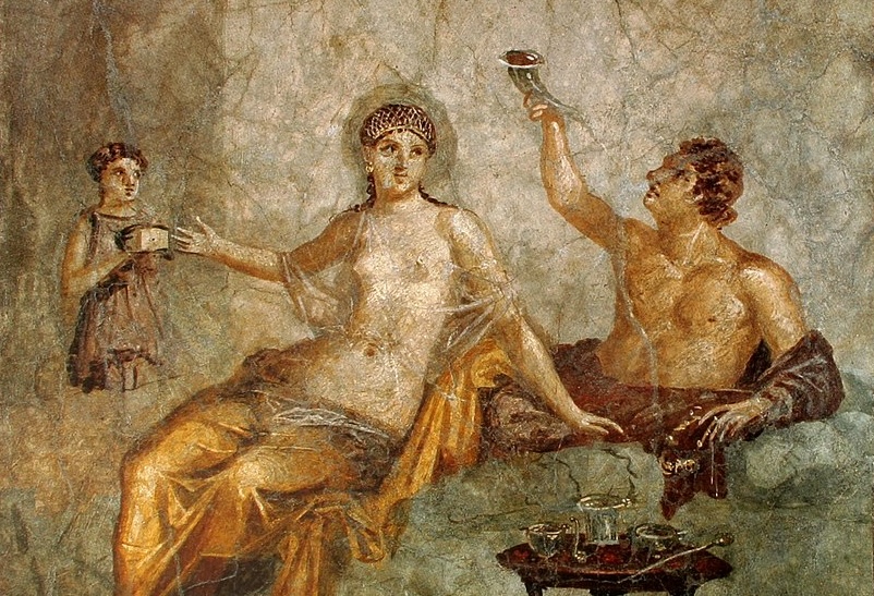 Una pareja romana disfruta de un banquete. Él está bebiendo de una copa con forma de cuerno y ella está alcanzando a una sirvienta que le trae una caja (¿quizás joyas?). 