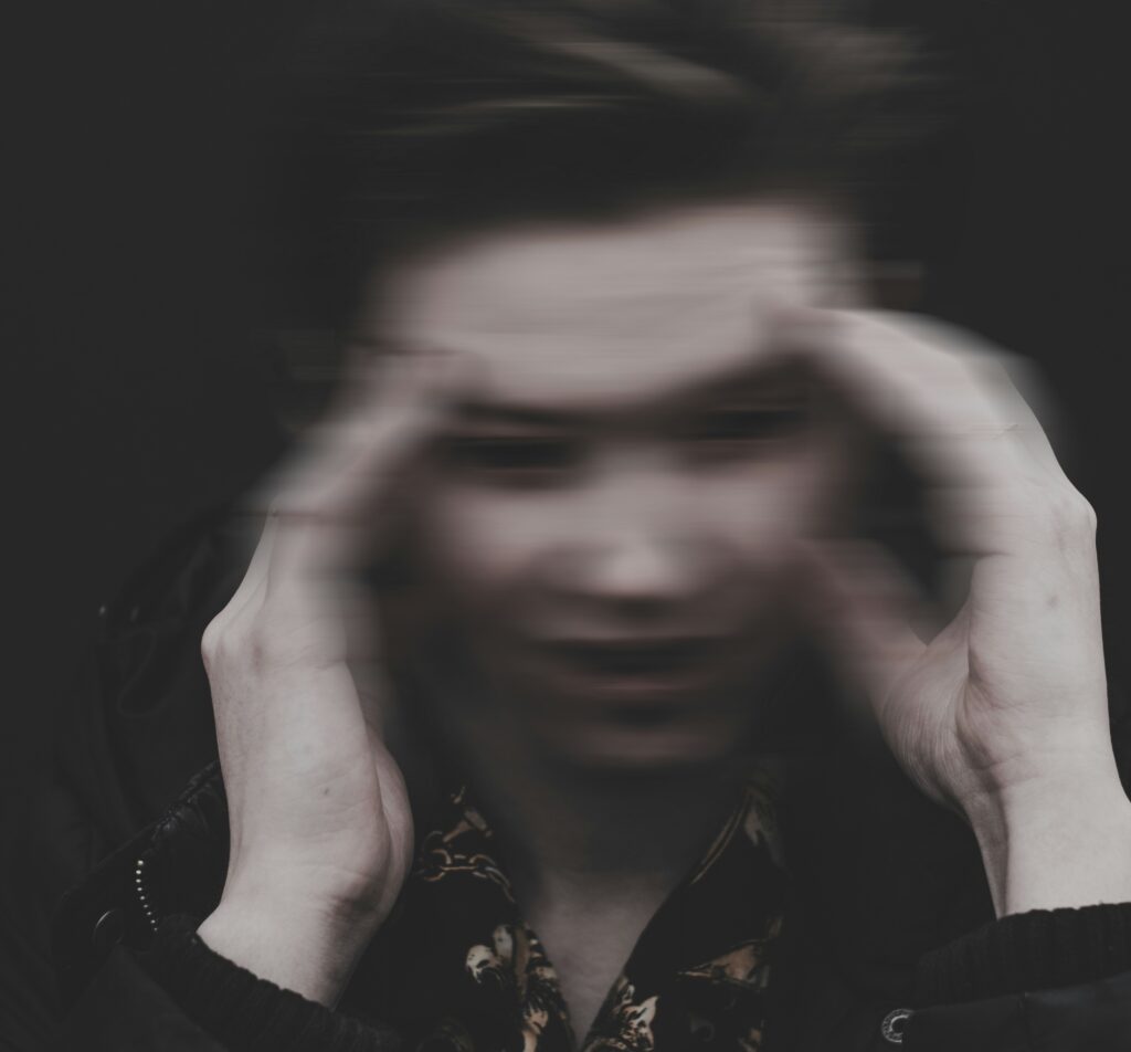 In this black and white photograph, a person holds their fingers to the temples of their forehead, as if in sorrow; their facial features are blurred.
